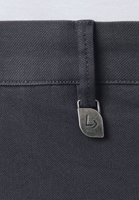 Czarny materiałowy pas z fakturowaną powierzchnią, z metalową metką z logo. Projekt obejmuje przeszytą pętelkę do zabezpieczania.