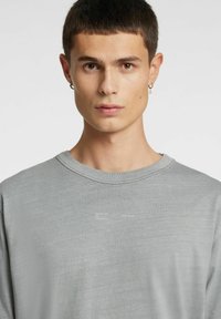 Jasnoszara koszula z długim rękawem, z okrągłym dekoltem, miękką fakturą i nadrukiem tekstowym na przodzie. Prosty i nowoczesny design.