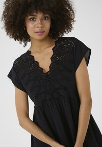 Black dress with short sleeves featuring intricate cut-out embroidery around the neckline; relaxed fit with a gathered waistline.