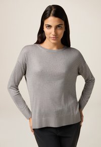 Hellgrauer Pullover mit langen Ärmeln, der ein strukturiertes Muster aus kleinen Löchern aufweist, sowie einen gerippten Halsausschnitt und Saum. Weiches Material mit lockerer Passform.