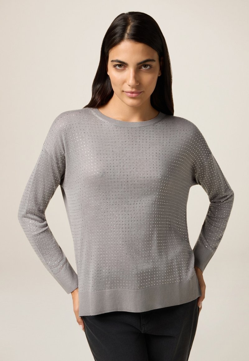 Hellgrauer Pullover mit langen Ärmeln, der ein strukturiertes Muster aus kleinen Löchern aufweist, sowie einen gerippten Halsausschnitt und Saum. Weiches Material mit lockerer Passform.