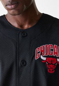 Black mesh baseball jersey featuring red embroidered "Chicago" text and a bull logo, with black buttons and a rounded neckline.