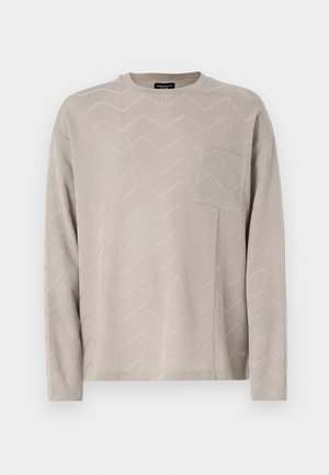 Light beige long-sleeve sweater with a textured zigzag pattern, featuring a square chest pocket and a round neckline.