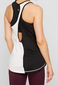 Top sin mangas en blanco y negro con diseño de espalda nadadora, detalle de espalda abierta y dobladillo curvado. Fabricado en una tela suave y elástica.