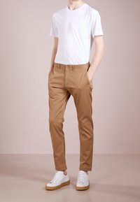 Tan cotton chinos with a straight-leg design, button closure, and side pockets, paired with a plain white crew-neck t-shirt and white sneakers.