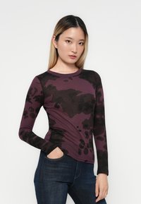 Lange mouw top in paars met een zwart camouflagepatroon, gemaakt van zachte stof met een aansluitende pasvorm en ronde hals.