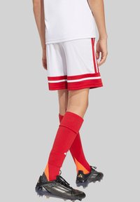Weiße Fußballshorts mit roten Streifen und passenden roten Socken, kombiniert mit schwarzen Fußballschuhen mit orangefarbenen Akzenten.