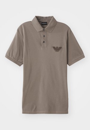 Short-sleeve polo shirt in taupe fabric, featuring a three-button placket and a textured emblem on the chest, with a classic collar.