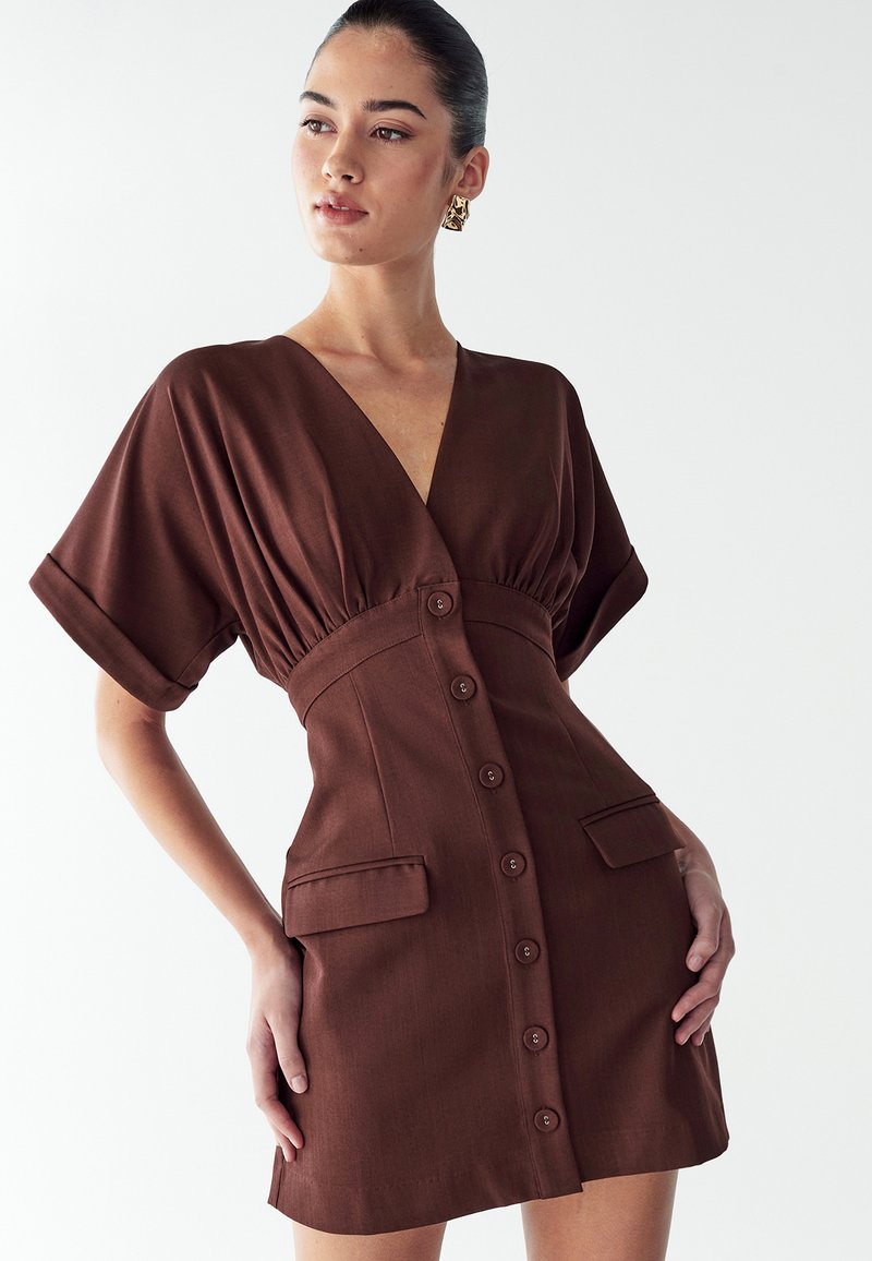 Robe marron à boutons avec un col en V, des manches courtes et une taille froncée. Comprend deux poches avant et un tissu lisse et texturé.
