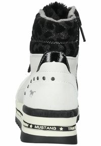 Baskets blanches et noires avec des accents imprimés léopard, doublure en fausse fourrure, détails brillants noirs et embellissements cloutés au niveau du talon.