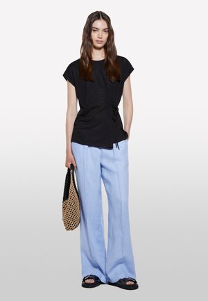 Haut noir à manches courtes avec détail froncé, pantalon large bleu clair, et sac en osier. Les sandales présentent un design de sangle simple.