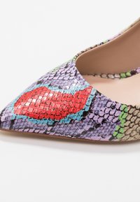 Chaussure à bout pointu avec un motif en cuir de serpent multicolore dans des nuances de violet, rouge et vert. Texture brillante avec une finition lisse.