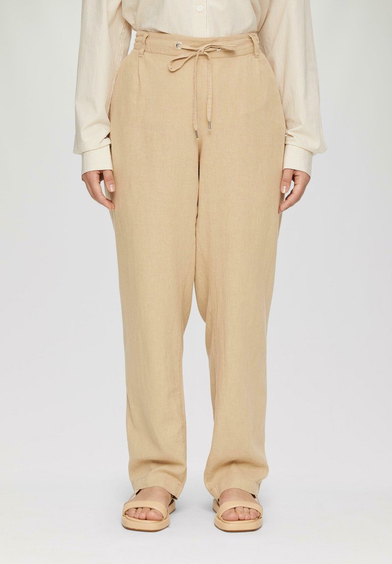 Beige linnen broek met een relaxte pasvorm, verstelbare tailleband en zijzakken. Gecombineerd met platte, open teend sandals.