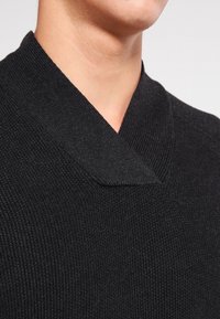 Svart stickad tröja med v-ringning. Har ett texturerat mönster och en subtil krage för extra dimension.