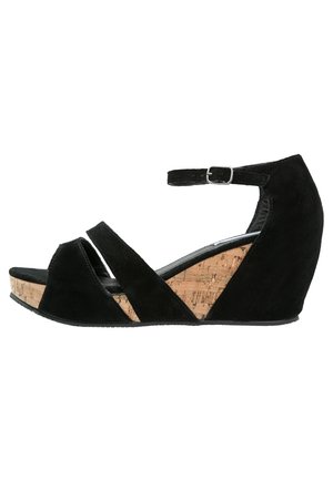 Sorte ruskind wedgesandal med en korkbund, der har krydsede stropper, ankelrem og åben tå-design. Glat tekstur med en veldefineret form.