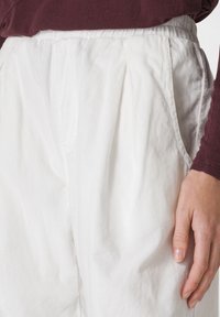 Pantaloni in corduroy bianchi con una finitura testurizzata, caratterizzati da pieghe e tasche laterali, abbinati a una maglietta lungo maniche color maroon.