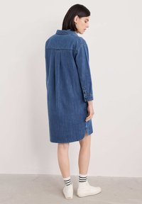 Jeansskjol i mörkblått med långa ärmar, knäppning med manschetter och en rundad nederkant. Har en bakre yoke och en avslappnad passform.