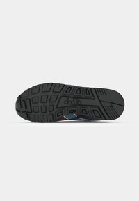 Sole of a sneaker featuring a patterned tread, with blue and maroon accents visible on the side. The background is plain white.