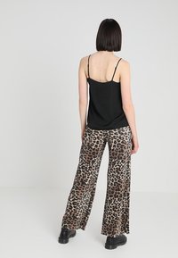 Top nero con spalline sottili abbinato a pantaloni larghi con stampa leopardata. I pantaloni presentano una texture liscia e una vestibilità ampia. Stivaletti neri alla caviglia.