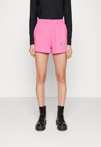 Růžové bavlněné šortky s elastickým pasem, na levé nohavici potisk "NIKE" a logo swoosh v bílé barvě. Černé šněrovací boty.