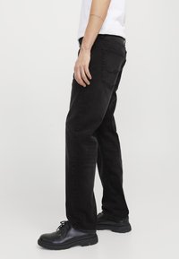 Jeans in denim nero con vestibilità dritta, trama sottile e tasche posteriori, abbinati a scarpe nere stringate. Design semplice e colore neutro.