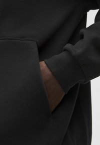 Fekete pulóver bordázott mandzsettával és elülső zsebbel. Puha, textúrált anyagból készült, amely kiemeli a tartósságot és a kényelmet.