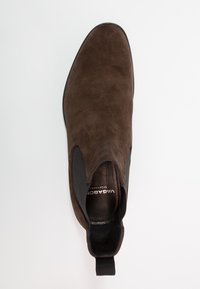 Botín Chelsea de ante marrón con paneles laterales elásticos, puntera redondeada y lengüeta en la parte posterior. Diseño elegante con detalles de hardware mínimos.