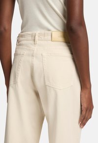 Pantalons beige clair en coton avec une coupe décontractée. Comprend deux poches arrière et une étiquette en cuir de marque sur la taille.