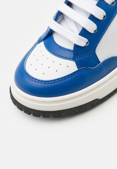Blauwe en witte sneaker met geperforeerde tenen, platte witte veters, rubberen zool en een glad leren bovenwerk. Heeft contrasterende stiksel.