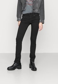 Svarta smala jeans kombinerat med en grå grafisk t-shirt och en svart denimjacka, kompletterat med svarta plattform ankle boots.