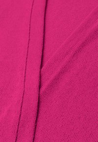 Lähikuva kirkkaan vaaleanpunaisesta teksturoidusta kankaasta, jossa näkyvät saumat ja pehmeän neulotun materiaalin yksityiskohdat.