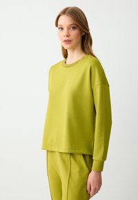 Sweatshirt vert citron avec une coupe décontractée, un col côtelé et une texture douce, associé à un pantalon tapered coordonné.