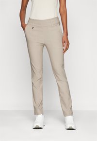 Beige, slim fit nadrág sima textúrával, magas derékkal, elülső zsebekkel és finom varrási részletekkel, fehér sportcipőkkel párosítva.