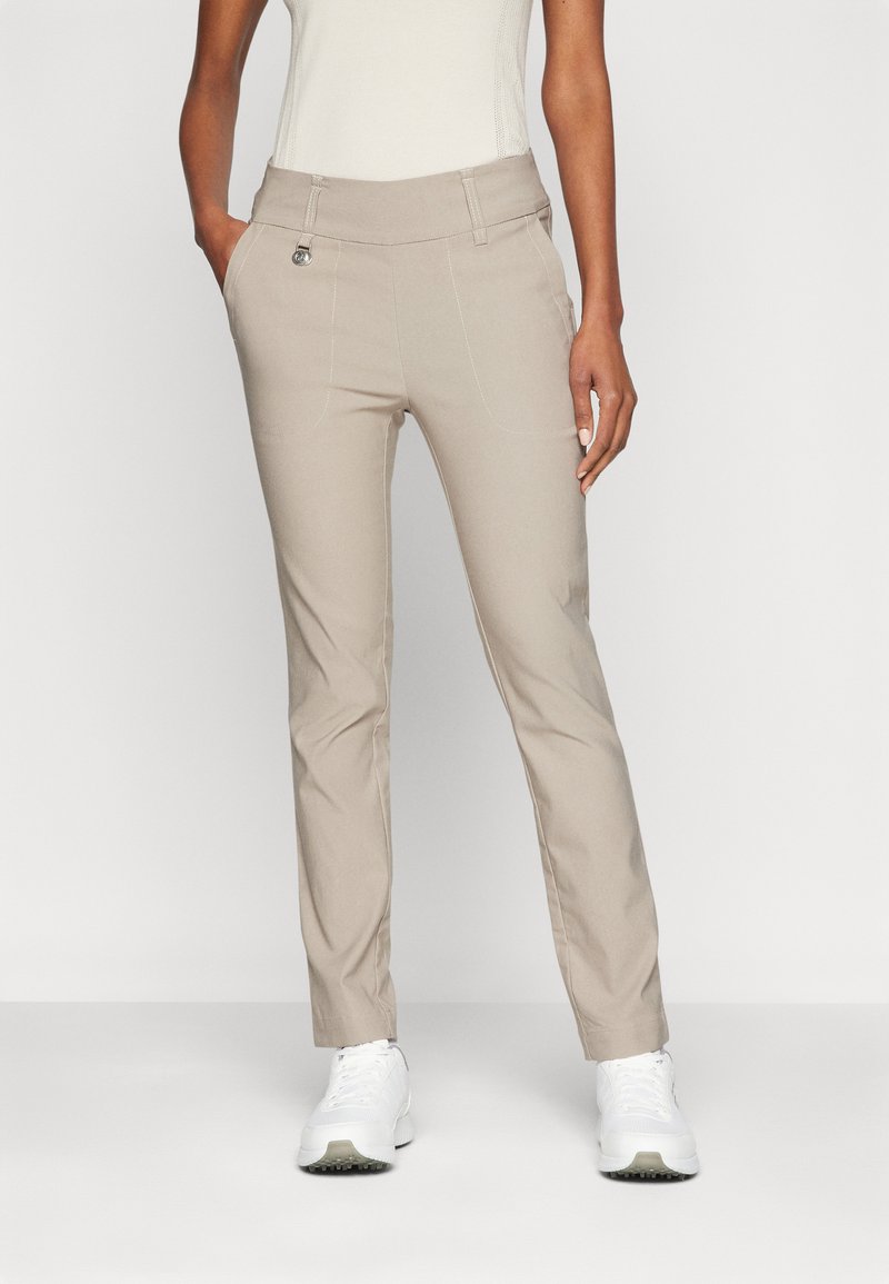 Beige, slim fit nadrág sima textúrával, magas derékkal, elülső zsebekkel és finom varrási részletekkel, fehér sportcipőkkel párosítva.