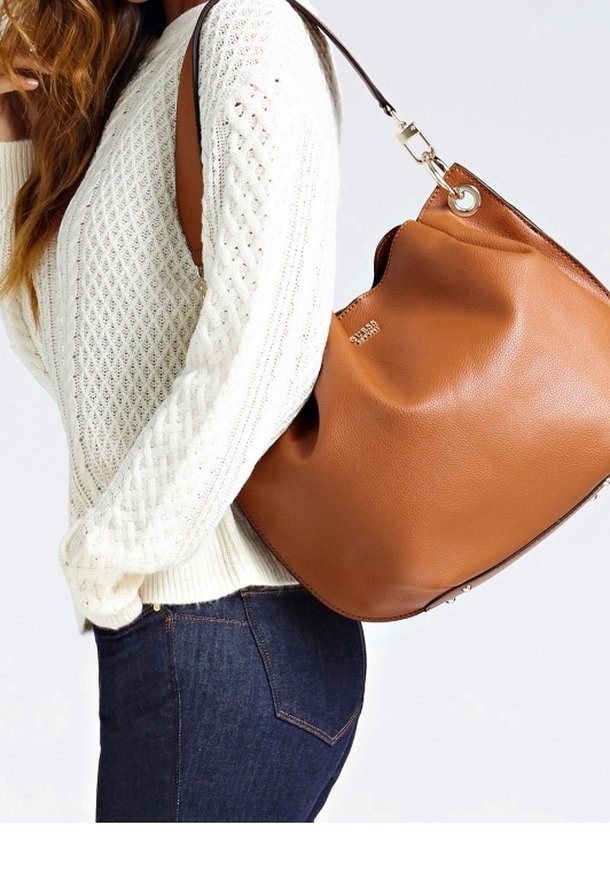 Femme portant un pull en maille blanc et un jean foncé, avec un grand sac à bandoulière en cuir marron avec des accessoires dorés.