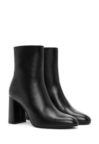 Botas de cuero negras hasta el tobillo con punta afilada y tacones altos en bloque. Textura suave, diseño minimalista y sin hardware ni embellishments visibles.