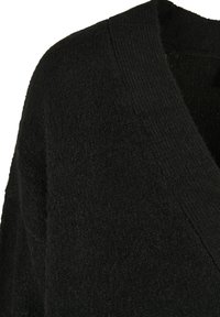 Cardigan en tricot noir avec une texture douce, un large col en V et un design à ouverture frontale. Le tissu semble épais avec une finition légèrement duveteuse.