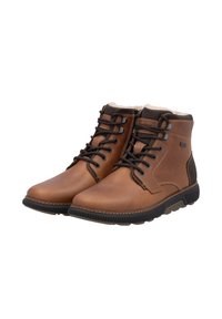 Bottes chelsea en cuir marron avec des accents marron foncé, design à lacets, col rembourré et semelle en caoutchouc texturée. Doublure en polaire visible en haut.