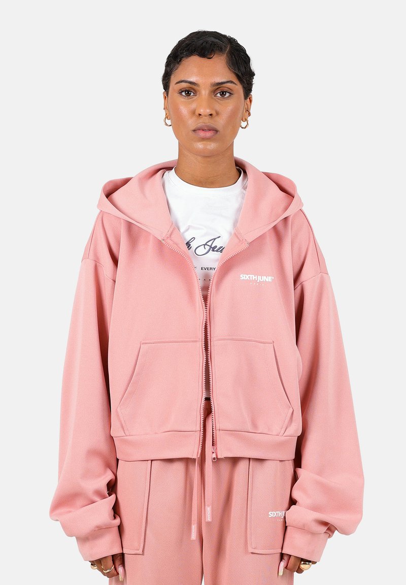 Sudadera con cremallera rosa, con un bolsillo frontal, cordón ajustable y logo visible. Tejido suave con un corte relajado y mangas oversized.
