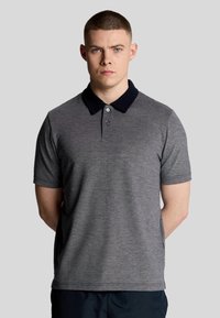 Grijze poloshirt van textuurstof, met een marineblauwe kraag, drie knopen en korte mouwen. Model staat recht voor zich uit.