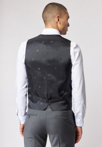 Schwarze gemusterte Weste mit satinierter Oberfläche, verziert mit kleinen Motiven, mit verstellbarem Rückenverschluss, getragen über einem weißen Hemd mit blauen Akzenten.
