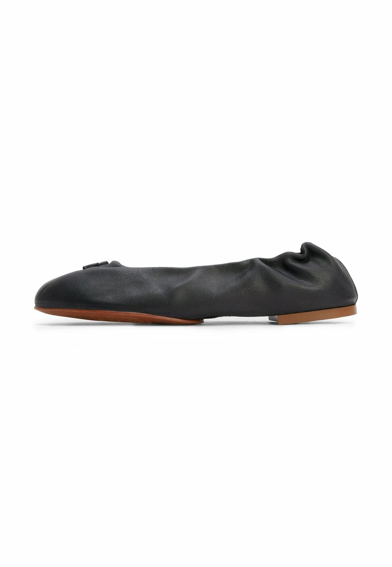 Ballerine plate en cuir noir avec texture froncée, bout rond et petit nœud en accent. Dispose d'une fine semelle marron.