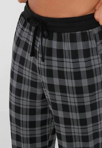 Zwarte en grijze geruite broek met een elastische tailleband en trekkoord. Zachte textuur, met een klassiek ruitpatroon.