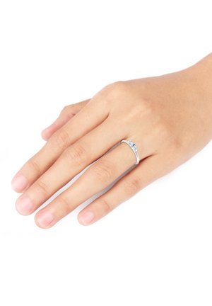 Silberring an einer Hand mit glatter Oberfläche, der ein einfaches Design und einen kleinen Edelsteinknopf in der Mitte aufweist. Der Hautton ist sichtbar.
