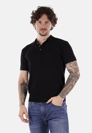 Camiseta polo negra de manga corta con textura acanalada, cuello de tres botones, costuras en contraste, combinada con jeans de mezclilla azules.