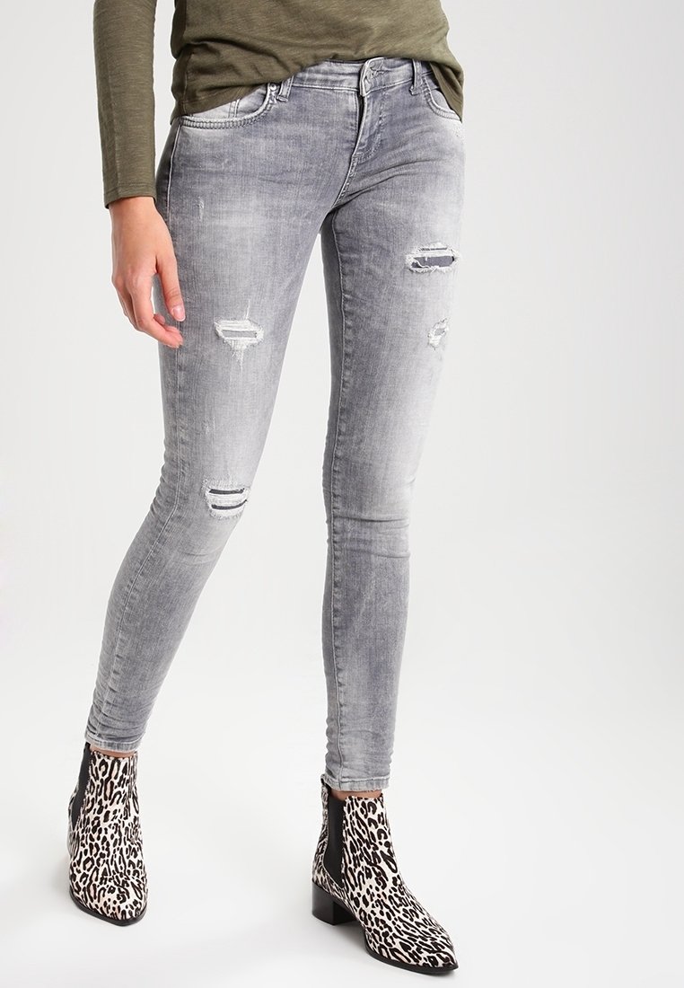 Jean skinny gris avec des déchirures usées et une texture lisse, associé à des bottines à imprimé léopard noir et blanc avec un talon bloc.