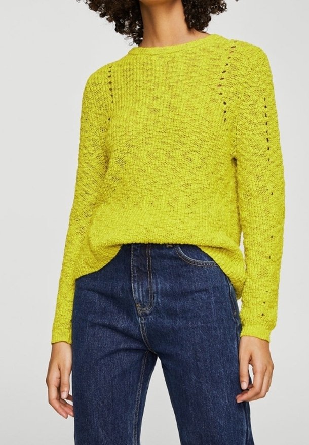Limonengrüner Strickpullover mit rundem Halsauschnitt, der an den Schultern mit offenem Strickmuster versehen ist, kombiniert mit dunkelblauen hochgeschnittenen Jeans.