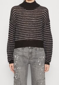 Maglione a strisce in bianco e nero con collo alto, maniche ampie e una vestibilità corta, abbinato a pantaloni grigi con macchie di vernice.