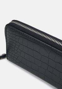 Black zippered wallet made of textured faux crocodile leather. Features silver zipper and black fabric trim. Rectangular shape with glossy finish.