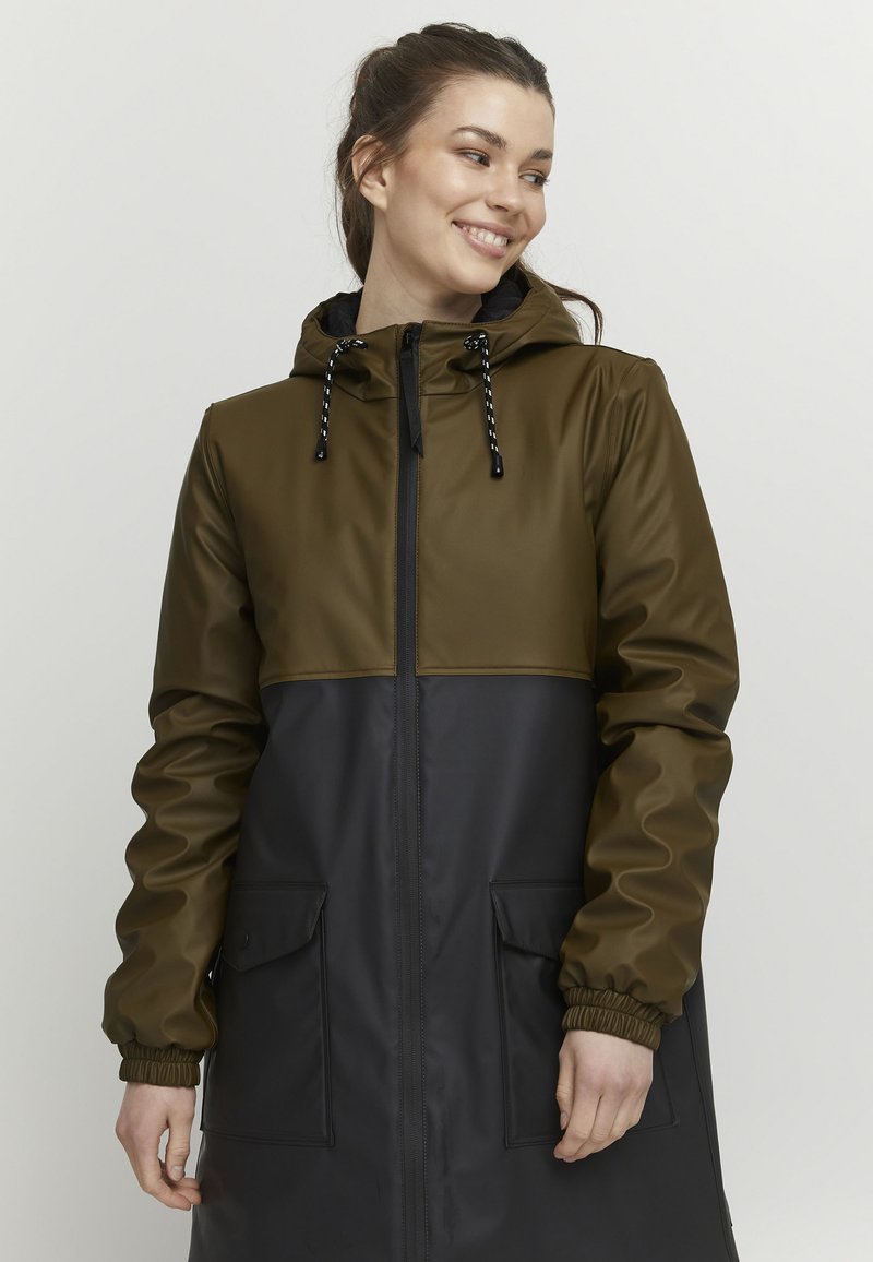 Manteau long en vert olive et noir, avec une capuche, fermeture éclair et grandes poches avant. Fabriqué en matériau lisse et imperméable.